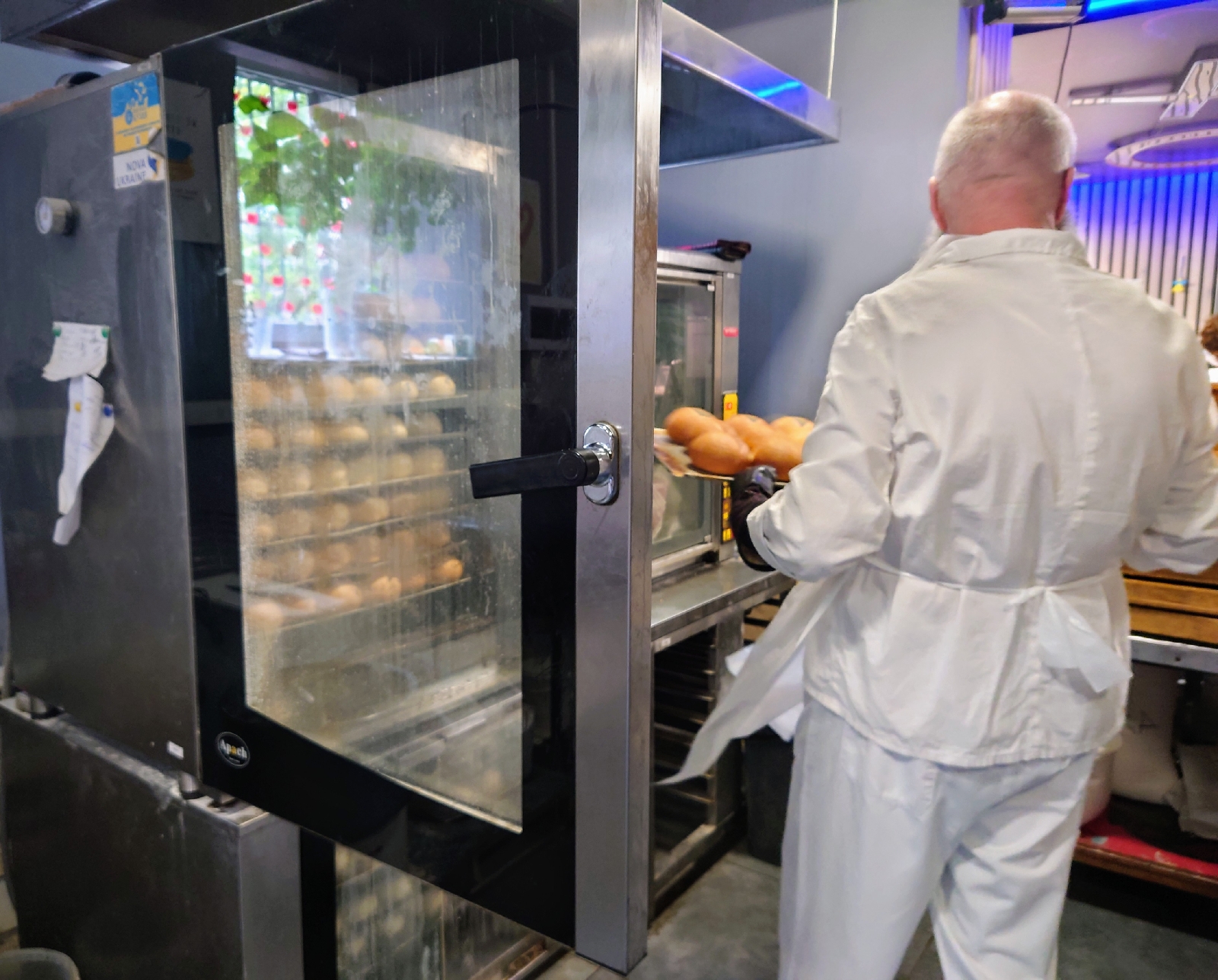 A baker loading a tray of fresh rolls into the oven